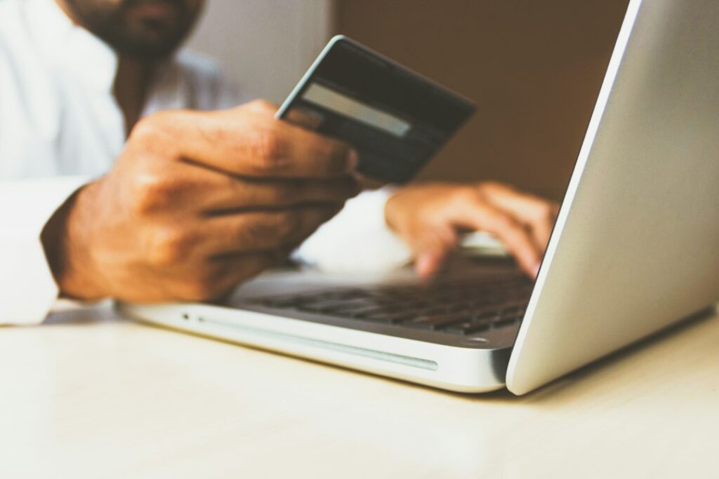 Person holding a payment card while using a laptop, illustrative stock photo