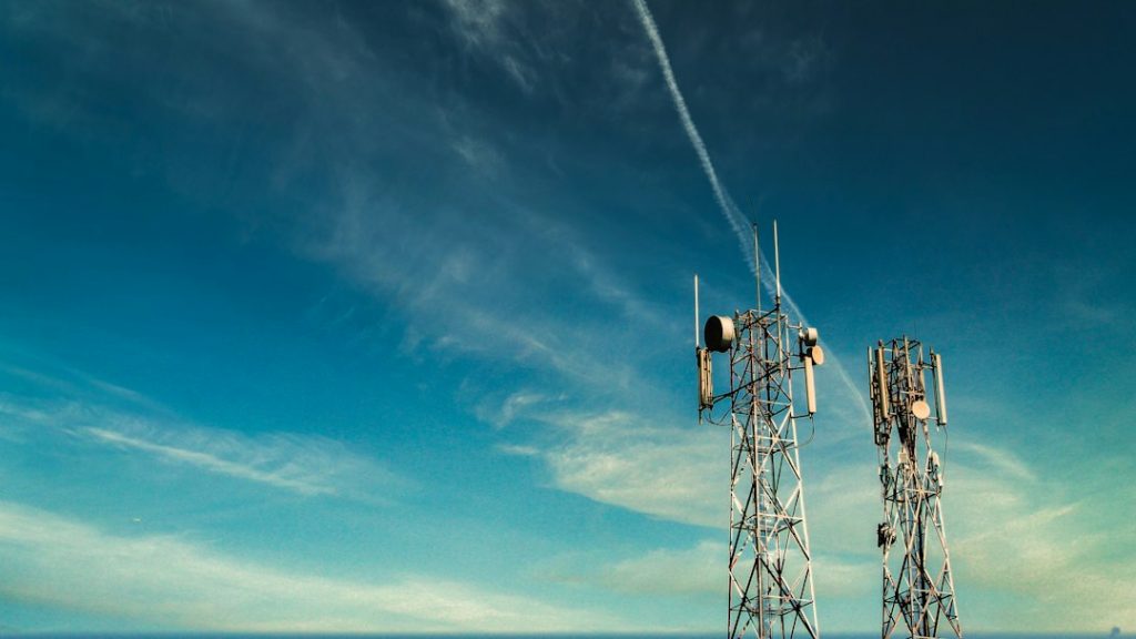 A telecommunications tower photographed from below against a blue sky.